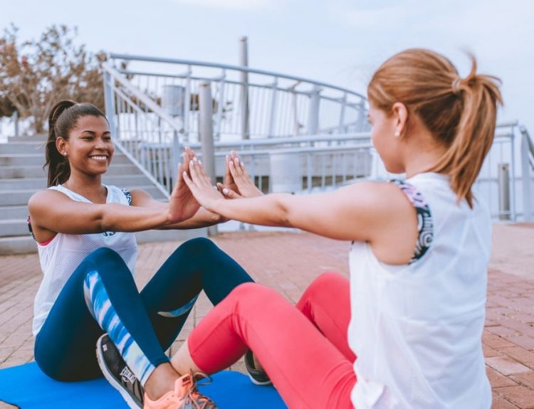 Two women exercising together outdoors, sharing a fun workout session with smiles and motivation.